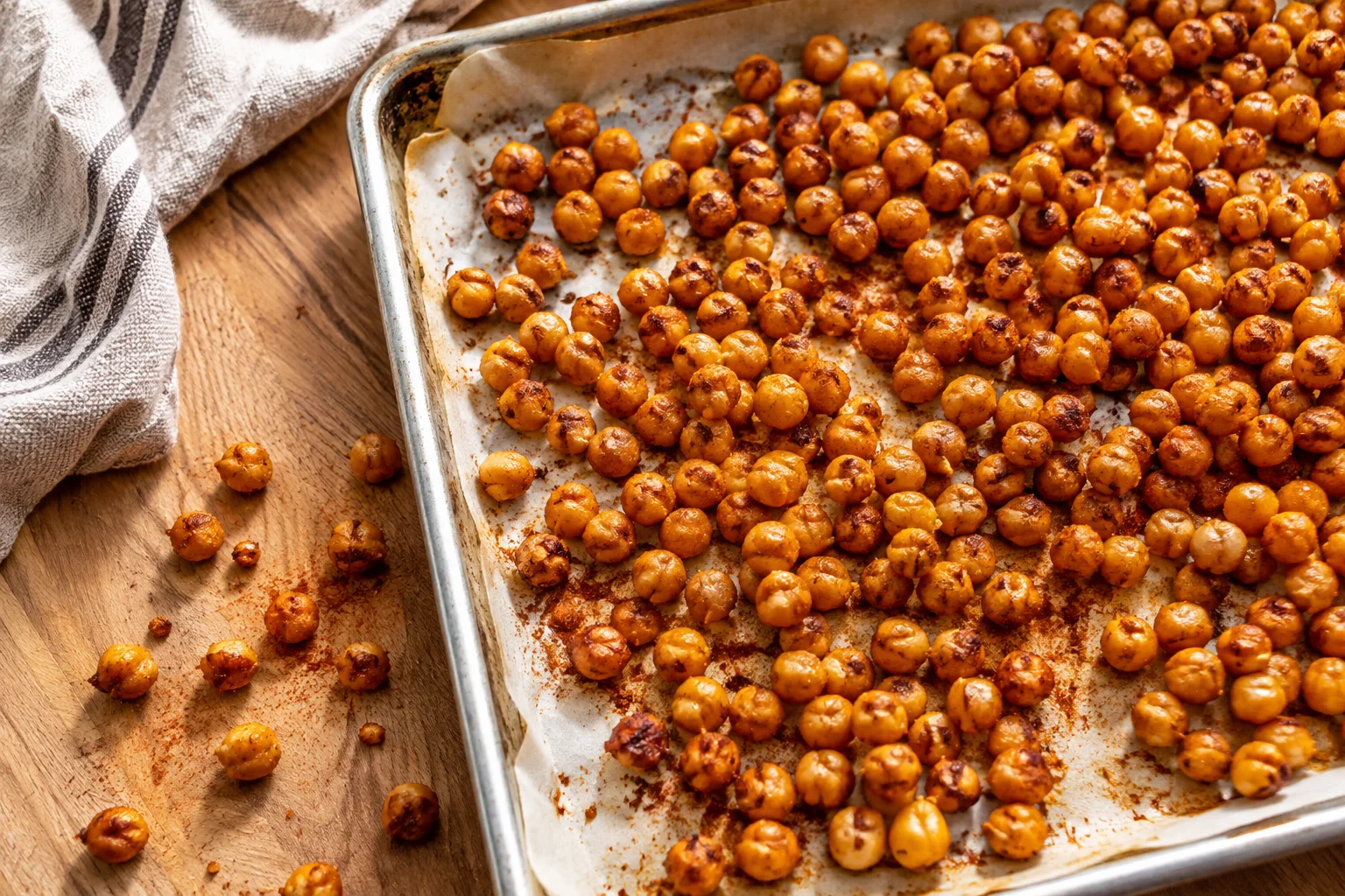 Rinsed canned chickpeas spread on a clean linen towel being patted dry with a hand, loose skins visible